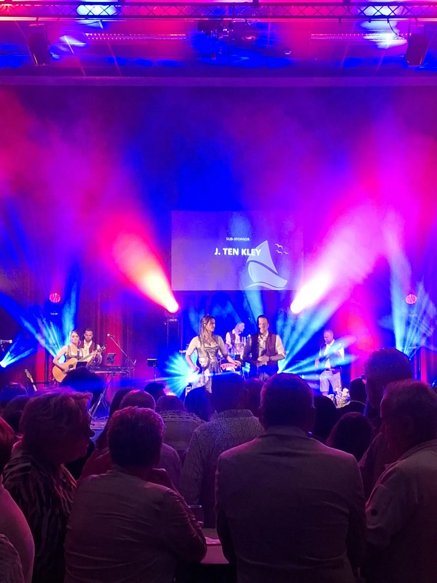Optreden op het podium van de Vaeszaal met publiek aan tafels